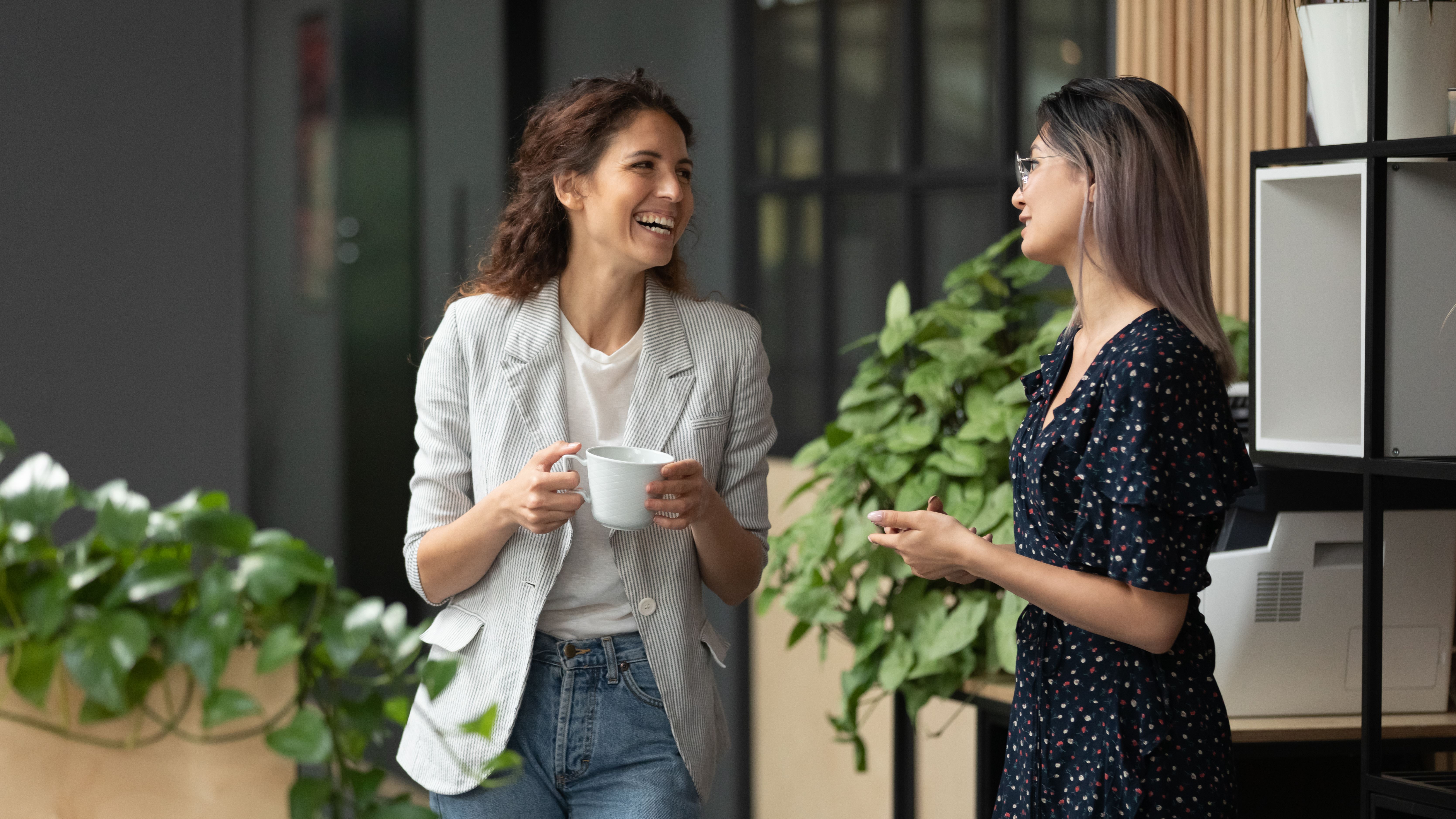 Twee vrouwen drinken koffie bij de printer en lachen met elkaar.
