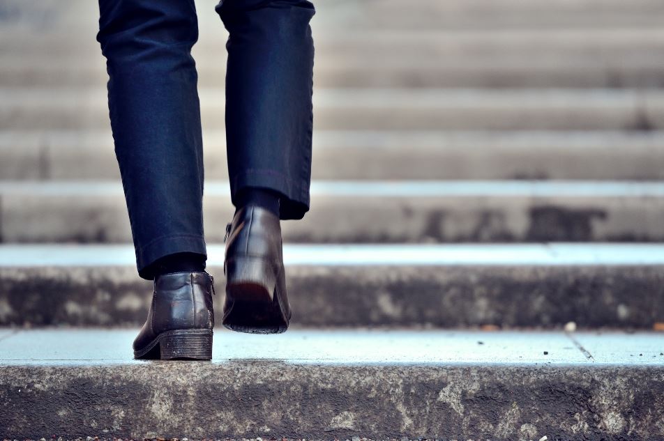 Een man met zwarte schoenen en een zwarte broek loopt een stenen trap op.