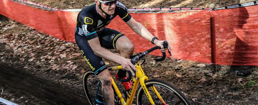 Veldrijder Corné van Kessel fiets op het wedstrijdparcours door de modder heen, op zijn gele fiets.