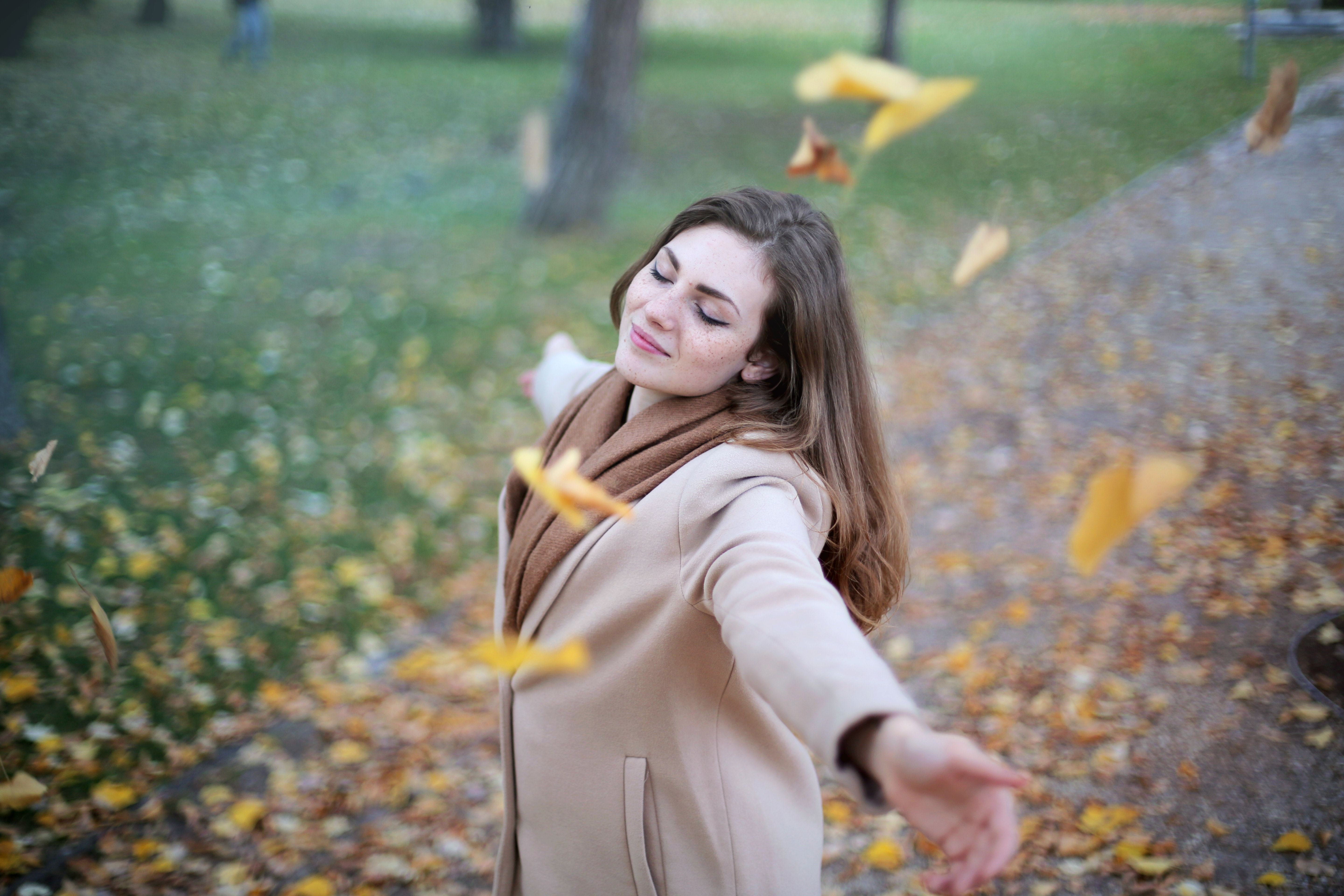 Jonge vrouw met bruin haar en sproetjes danst in vallende blaadjes in een park