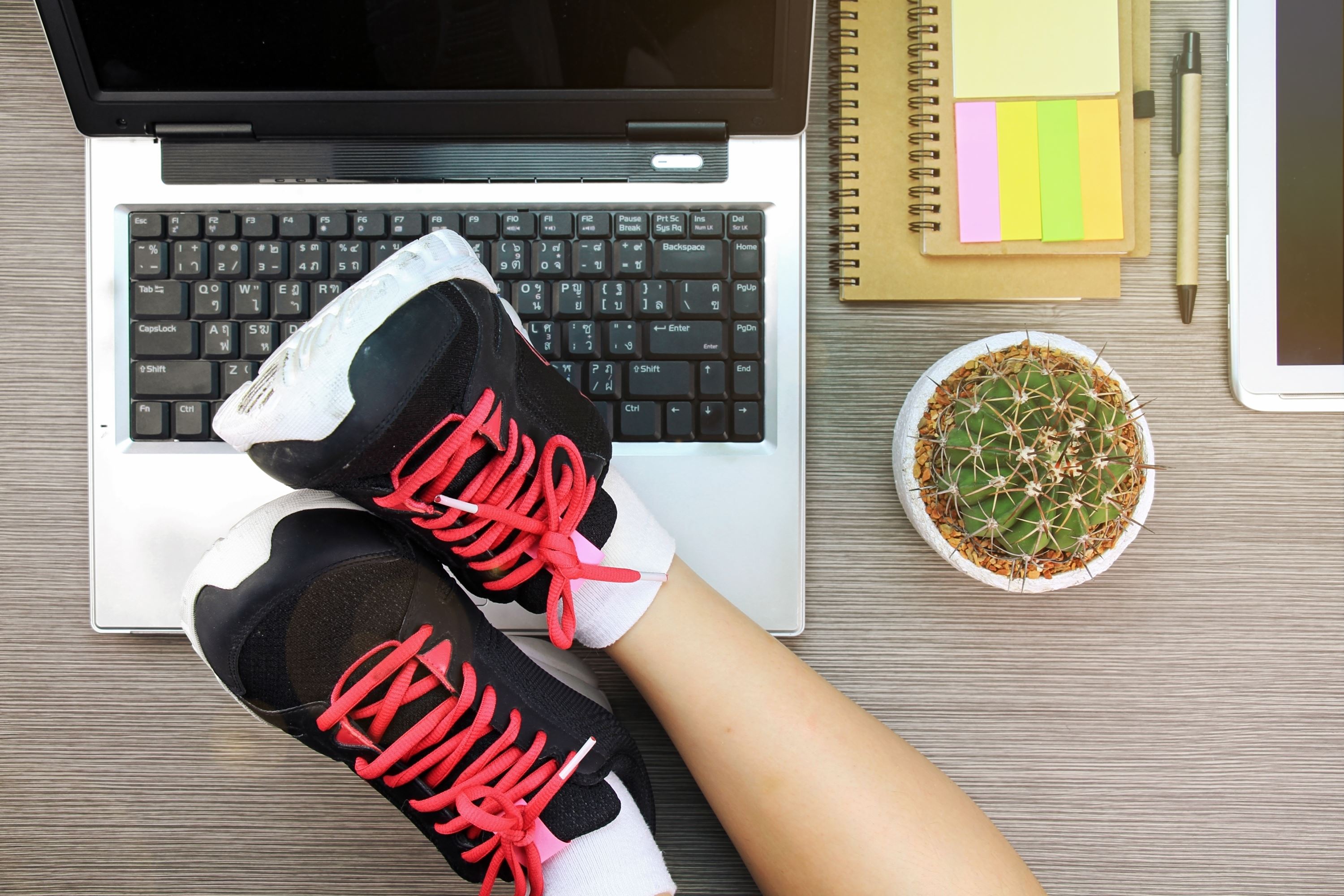 Een vrouw ligt met haar sportschoenen op haar opengeklapte laptop.