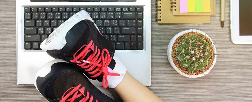 Een vrouw ligt met haar sportschoenen op haar opengeklapte laptop.