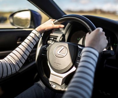 Vrouw met wit-zwart gestreept lange mauwen shirt zit met handen aan het stuur in een Lexus