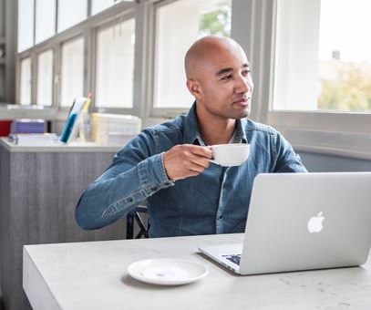 Een man werkt op zijn laptop en drinkt een kopje koffie.