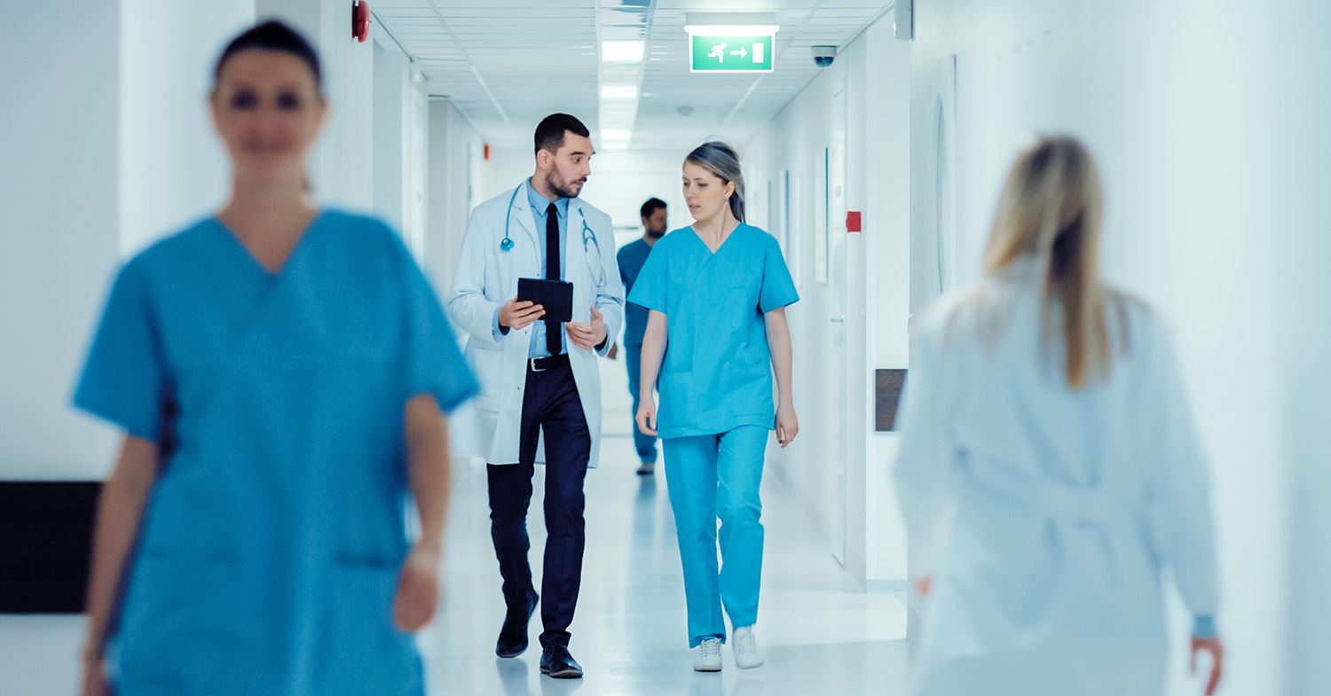 Een mannelijke dokter en vrouwelijke assistent lopen samen door een gang in het ziekenhuis.