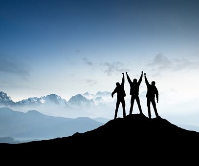 Drie mensen staan op een berg, de mensen hebben alle drieën handen in de lucht en juichen.