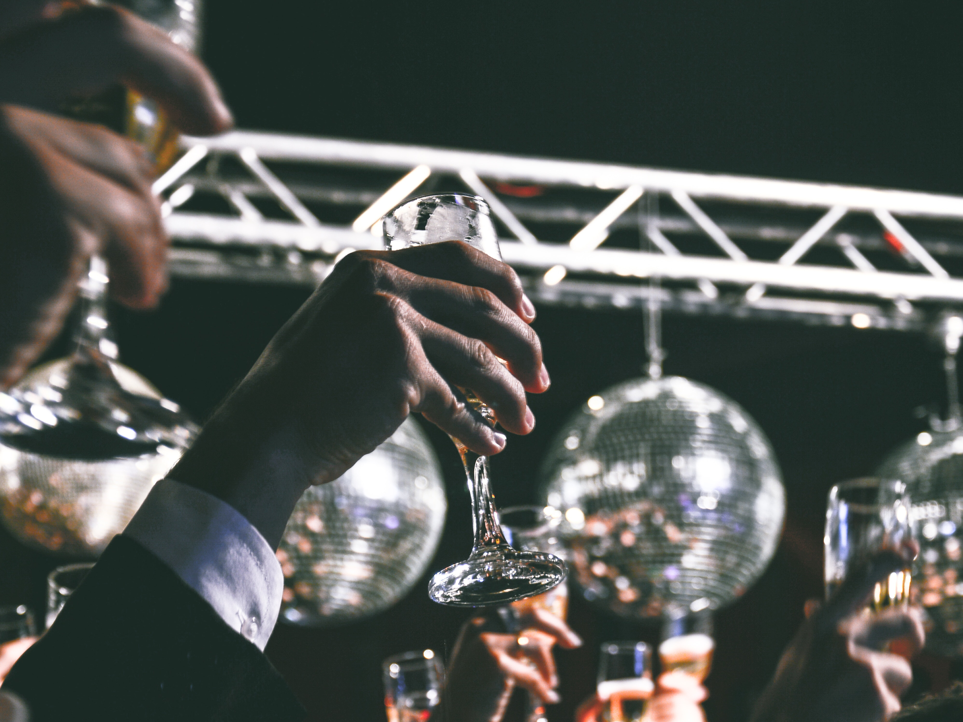 Een groep mensen heffen hun glas op een feest, op de achtergrond hangen discoballen.