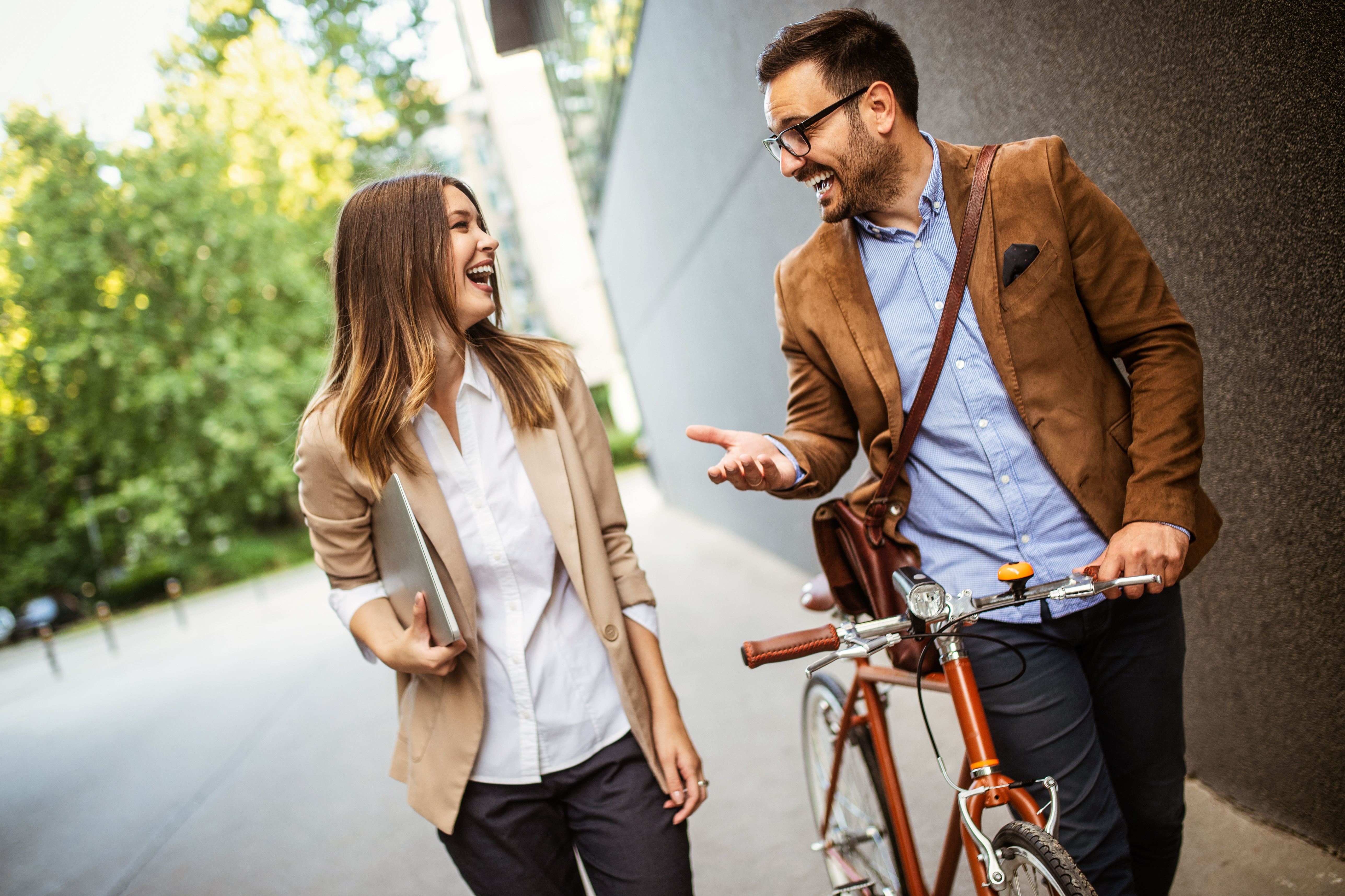 Een man en een vrouw lopen over straat, de man heeft een rode fiets in de hand. De twee mensen lachen naar elkaar