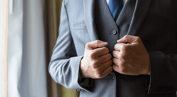 Man in grijs pak en blauw met wit gestipte stropdas die zijn dichtgeknoopte jasje vastpakt