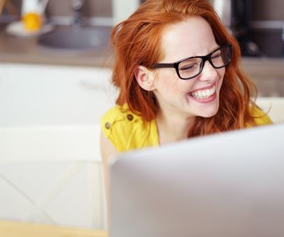 Een vrouw met rode haren zit achter haar computer en lacht.