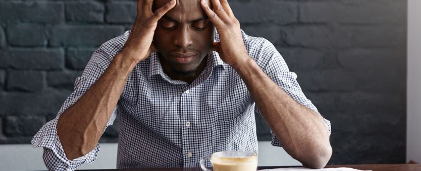 Een man zit gefrustreerd achter zijn bureau, op zijn bureau staat een laptop en een kopje koffie.