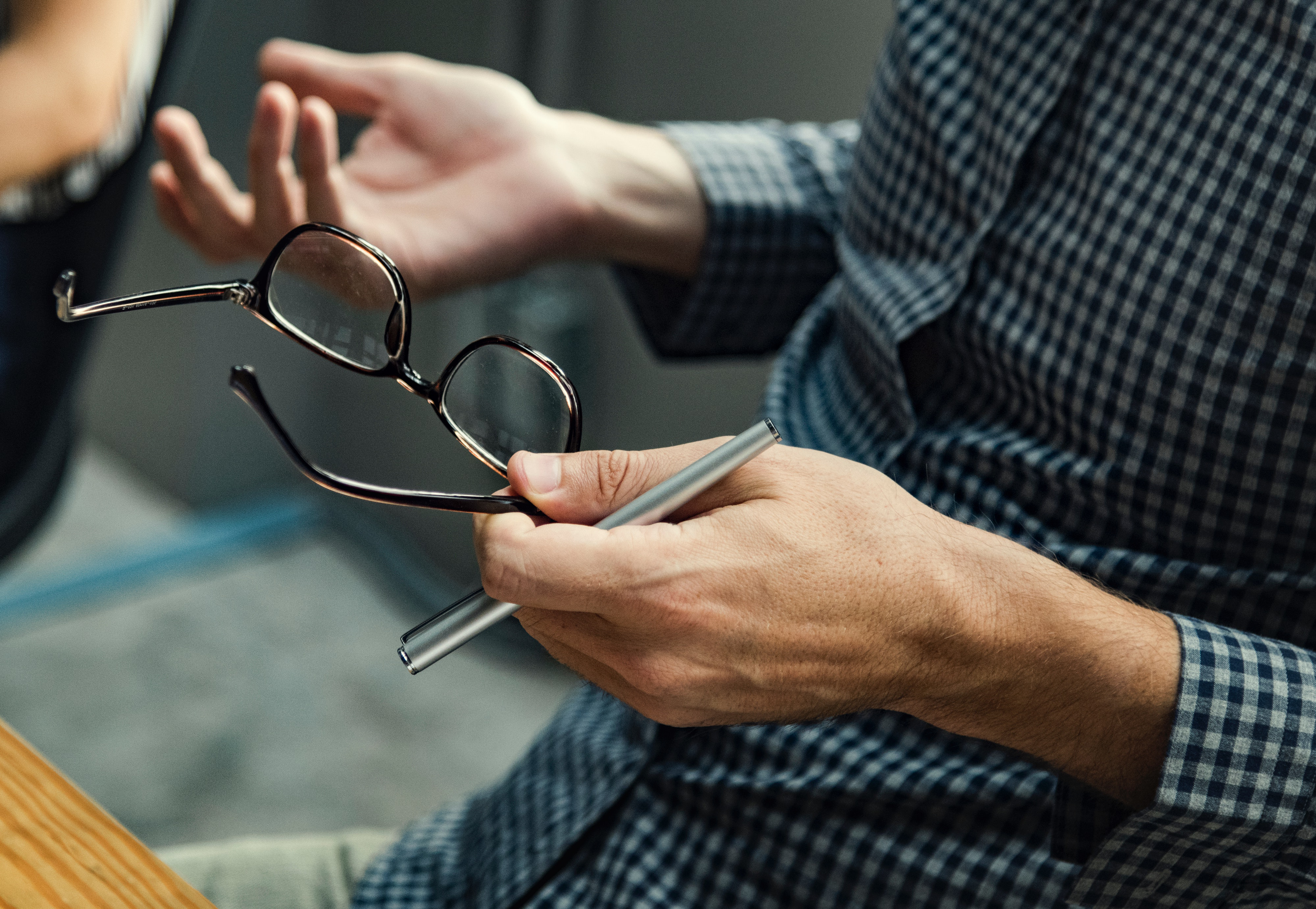 Een man heeft zijn bril en een pen in zijn handne terwijl hij met zijn handen praat.