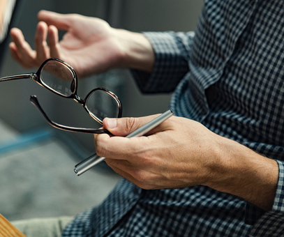 Een man heeft zijn bril en een pen in zijn handne terwijl hij met zijn handen praat.