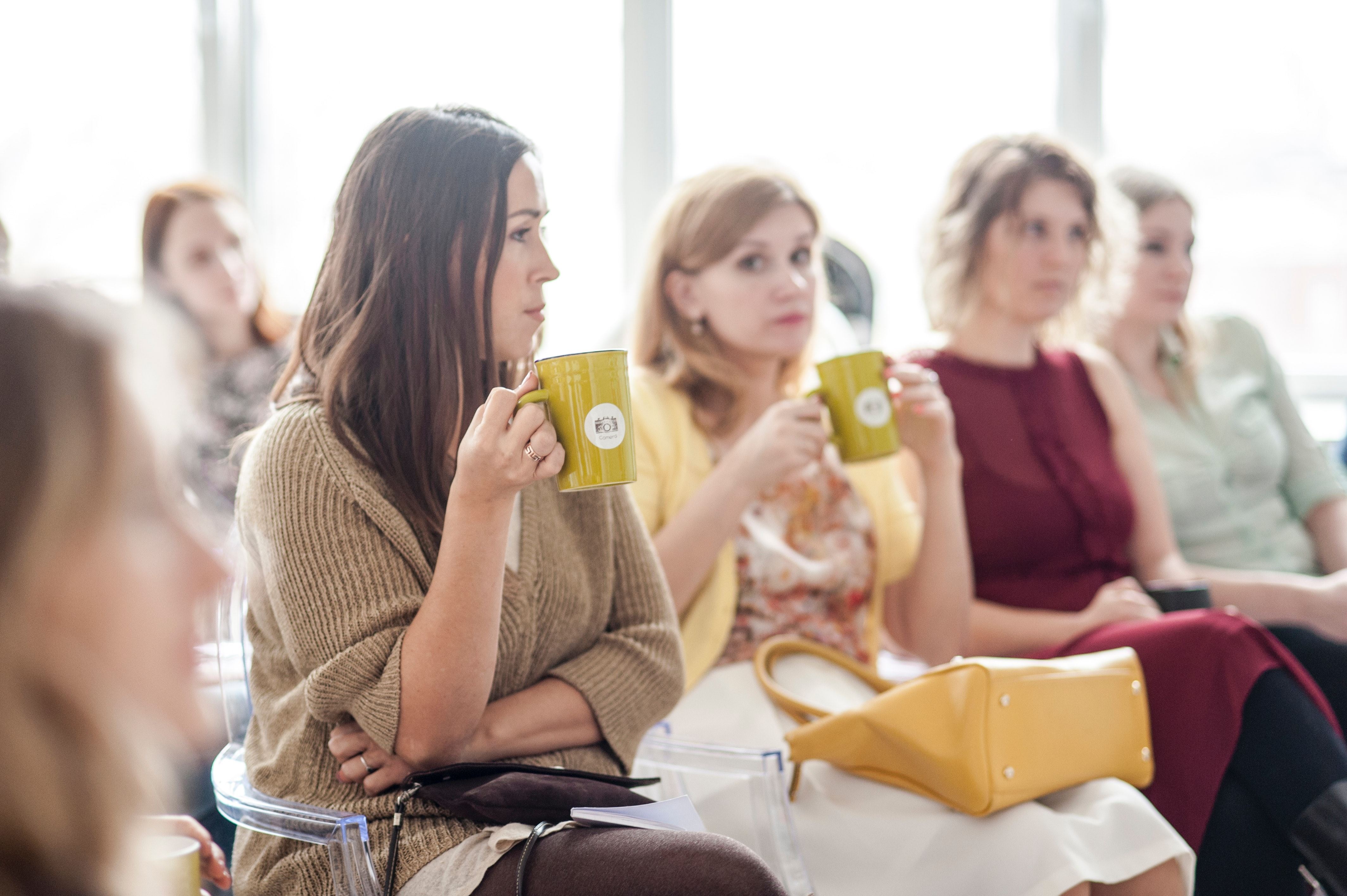 Zaal vol met vrouwen waarvan twee vrouwen thee drinken uit een groene mok