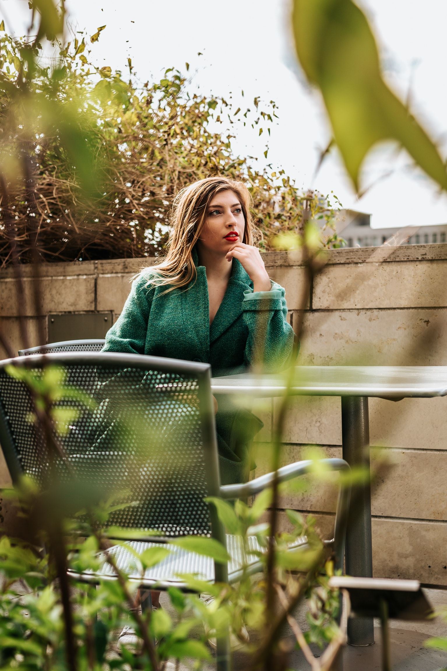 Vrouw met groen vest zit nadenkend op dakterras met planten