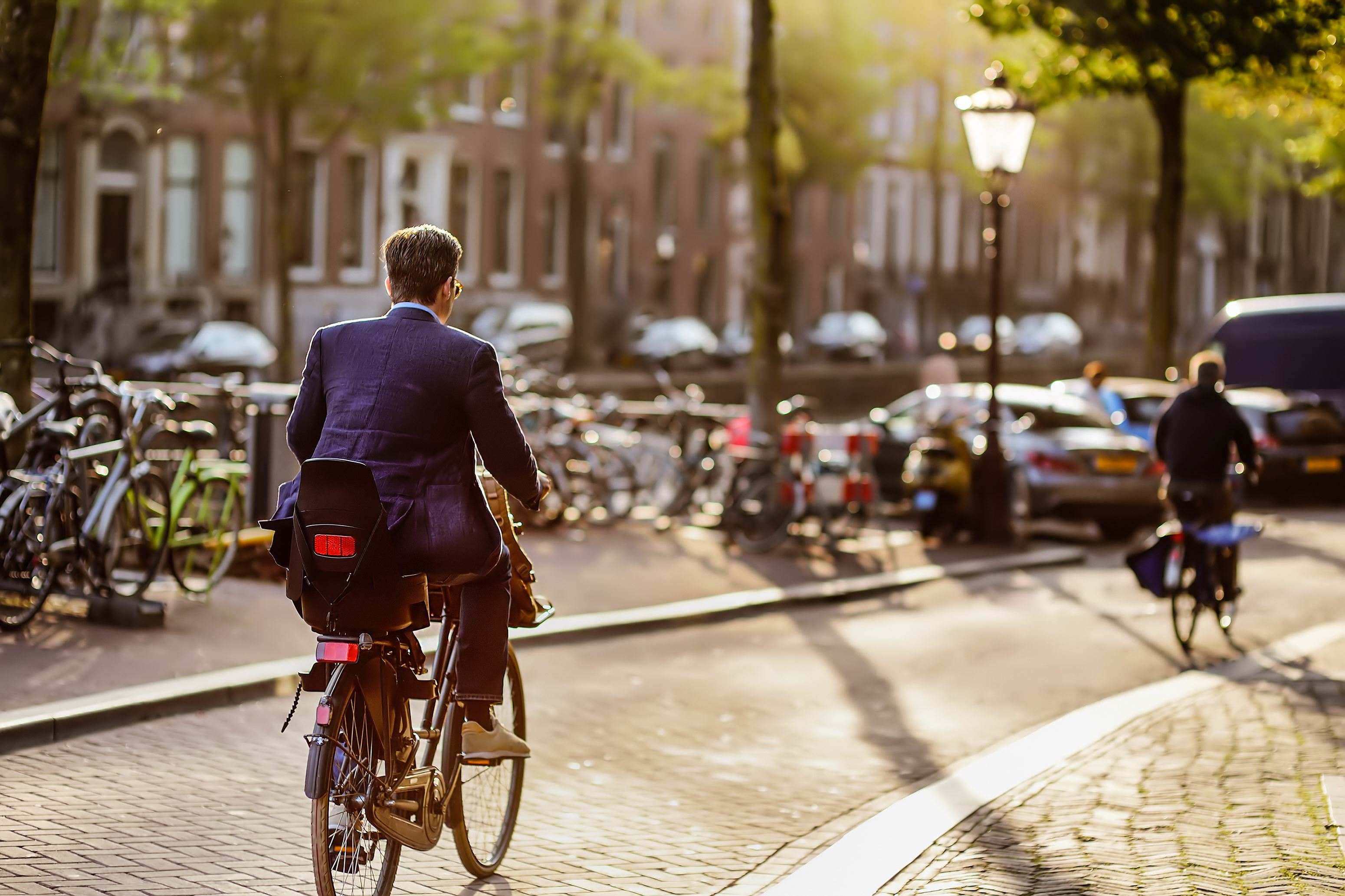 Een man in professionele kleding fietst weg van de camera over straat in de stad in een zonnige setting.