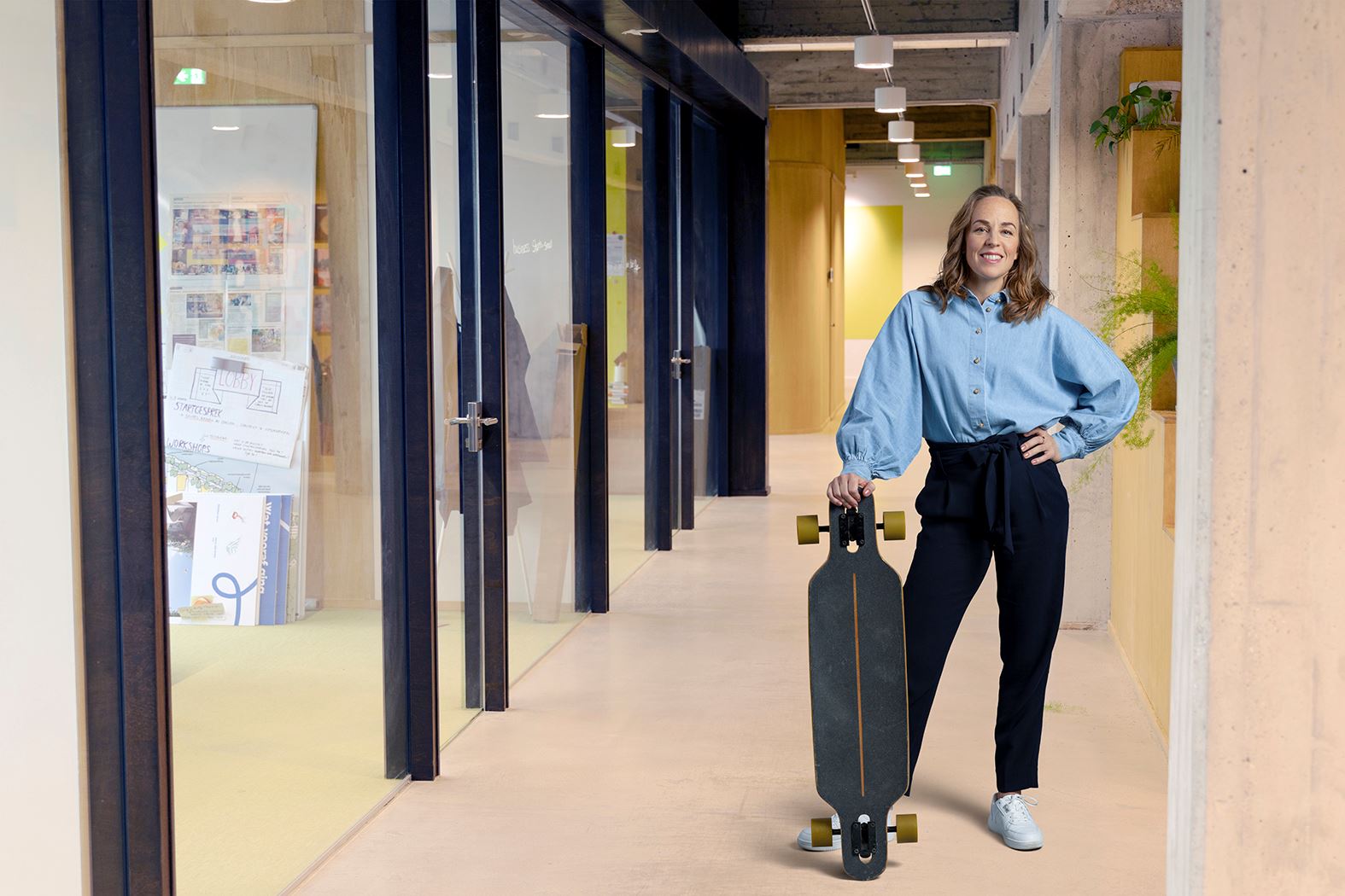 Een vrouw staat met een longboard in een kantorenpand.