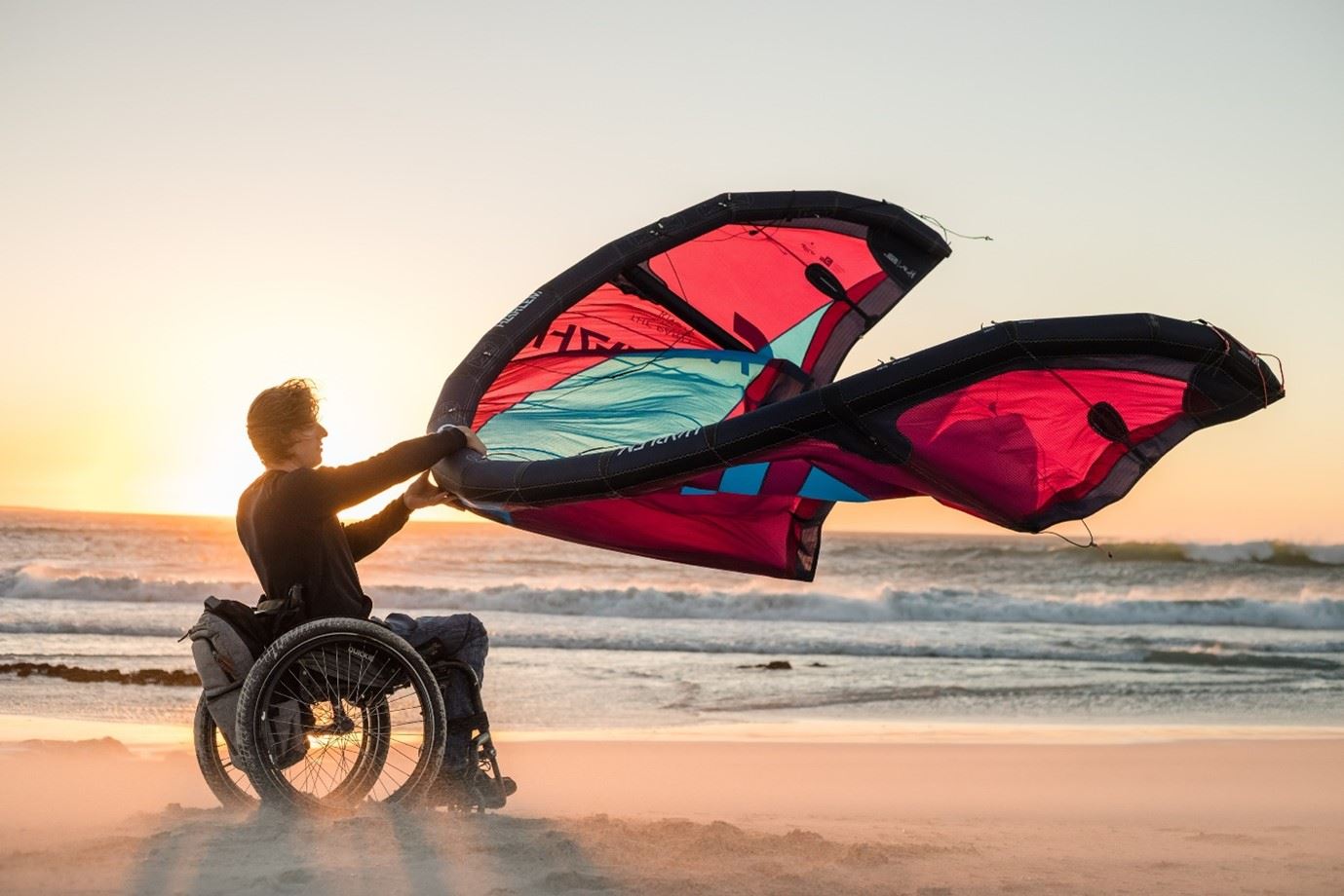 Willem Hooft, een man in een rolstoel, op het strand met een paraglider in zijn handen.