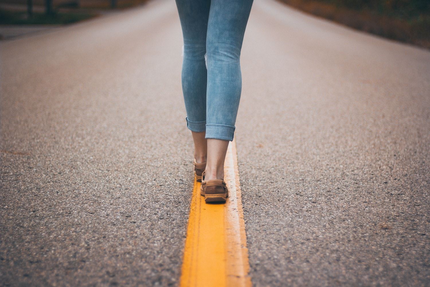 Een vrouw loopt midden op een verlaten weg op een gele streep.