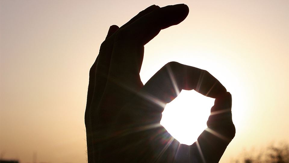 Een man heeft zijn hand in de vorm van een rondje waar de zon doorheen schijnt.