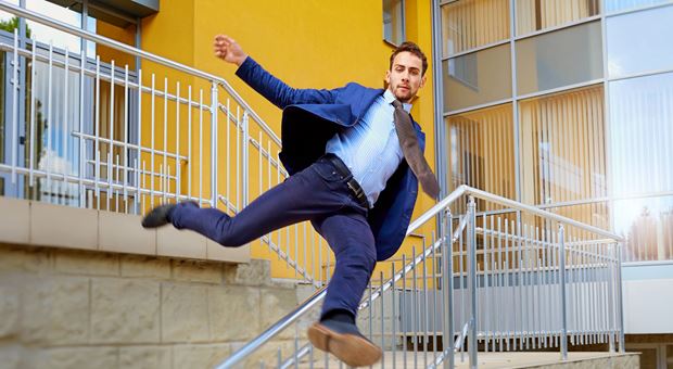Een man in een blauw net pak springt over een reling van de trap af. De man heeft een gele met zwart gestreepte stropdas