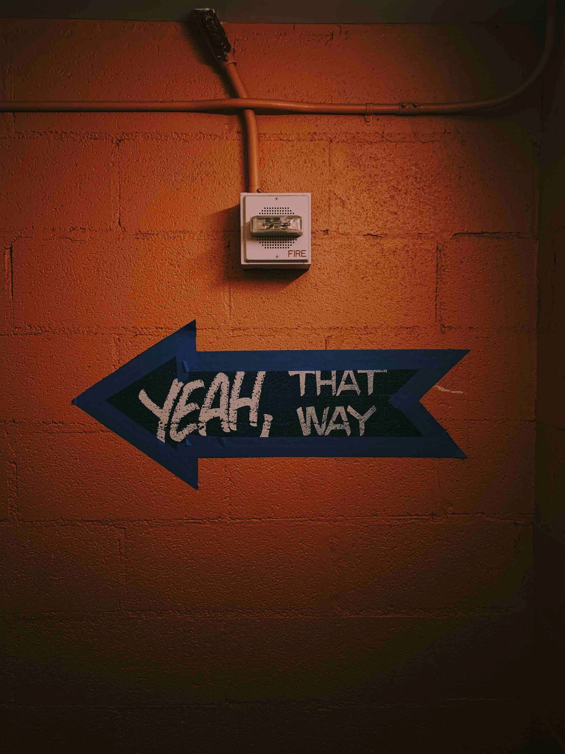 Een blauwe pijl op een rode muur waar: ''yeah, that way'' op staat.