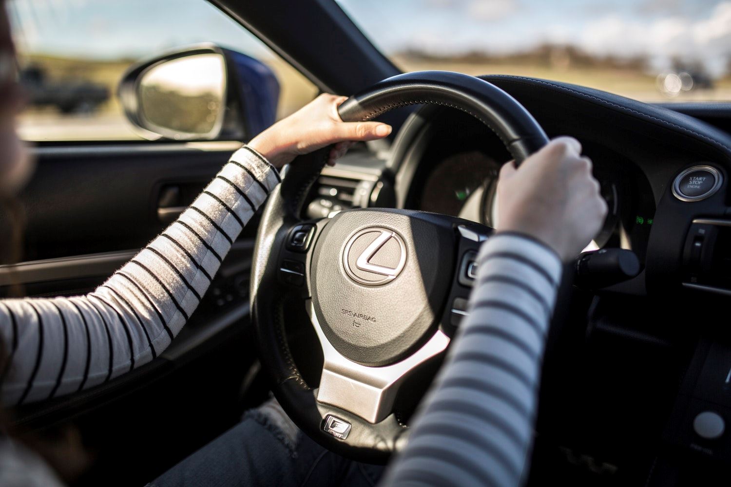 Een vrouw met een wit en zwart gestreept shirt heeft haar handen op het stuur van de auto.