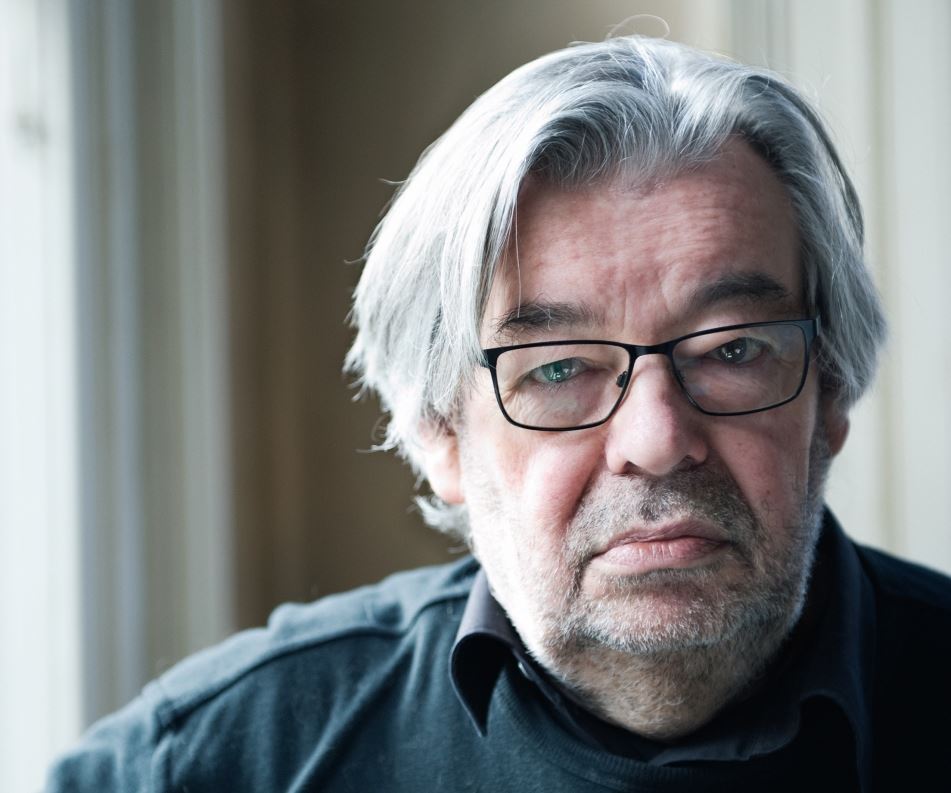 Een close-up van Maarten van Rossum, een man met grijze haren en een zwarte bril.