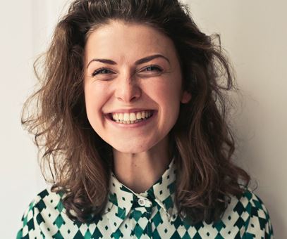 Een vrouw met bruine haar met een grote glimlach op haar gezicht die voor een witte muur staat