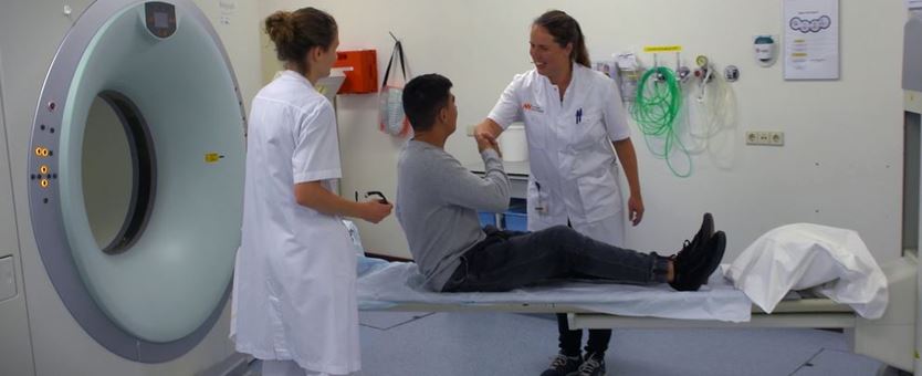 Een man ligt op een ziekenhuis bed voor een mri-scan. Hij geeft een hand aan een vrouwlijke doktor.