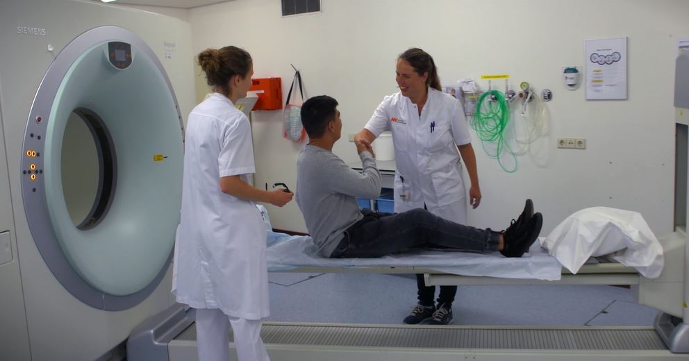 Een man ligt op een ziekenhuis bed voor een mri-scan. Hij geeft een hand aan een vrouwlijke doktor.